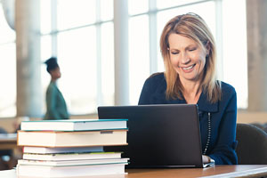 Une femme utilise un ordinateur portable tout en étant assise à un bureau rempli de manuels scolaires.
