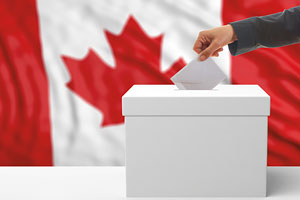 A person places a ballot into a box in front of the Canadian flag.