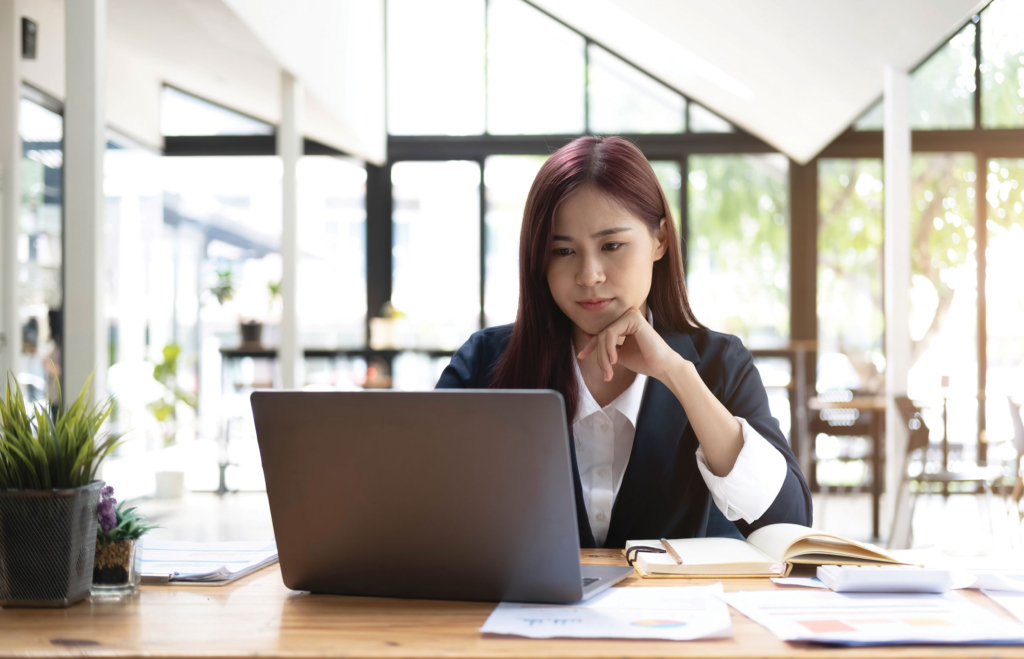 A woman sits at a desk in front of a laptop.